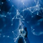 Mão robótica alcança uma rede digital iluminada sobre fundo azul, em representação conceitual da inteligência artificial.