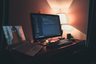 Escritório doméstico com dois monitores exibindo um ambiente de programação e desenvolvimento de software.