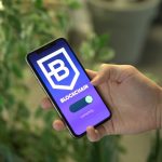 Mão segurando um smartphone que exibe uma interface de aplicativo de blockchain.