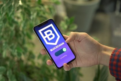 Mão segurando um smartphone que exibe uma interface de aplicativo de blockchain.