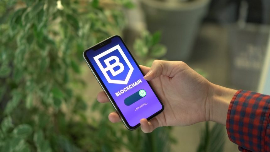 Mão segurando um smartphone que exibe uma interface de aplicativo de blockchain.